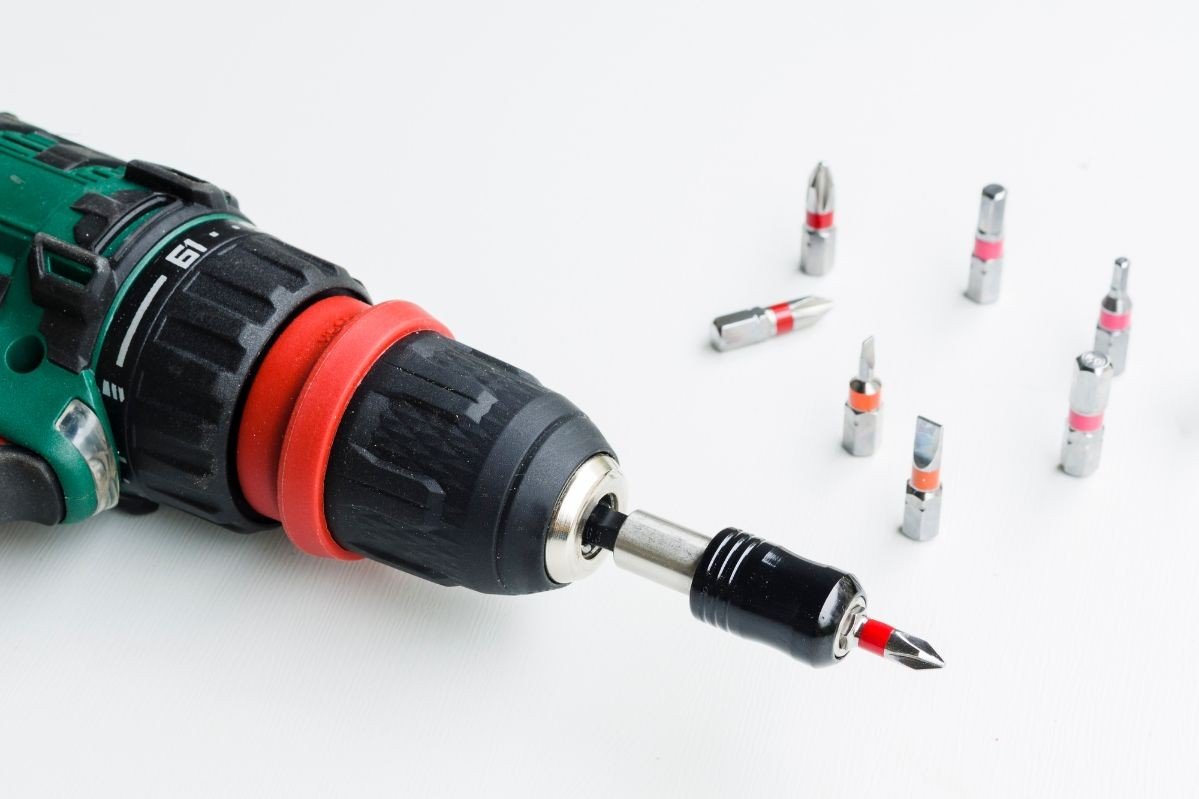 parafusadeira com algumas ponteiras ao lado em cima de mesa branca